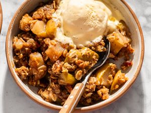 A bowl of apple crisp topped with ice cream and a spoon resting inside