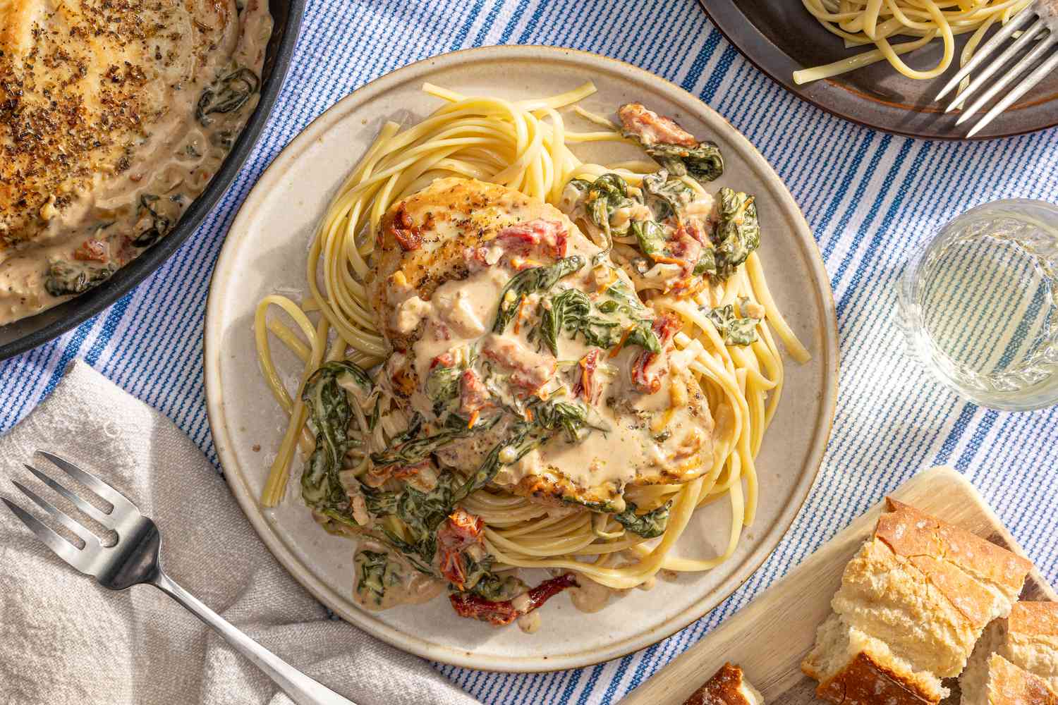 creamy tuscan chicken served over rice at a table setting with more in a pot, bread on a wooden board, and utensils