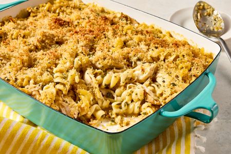A casserole dish containing chicken piccata noodle casserole with a serving spoon nearby