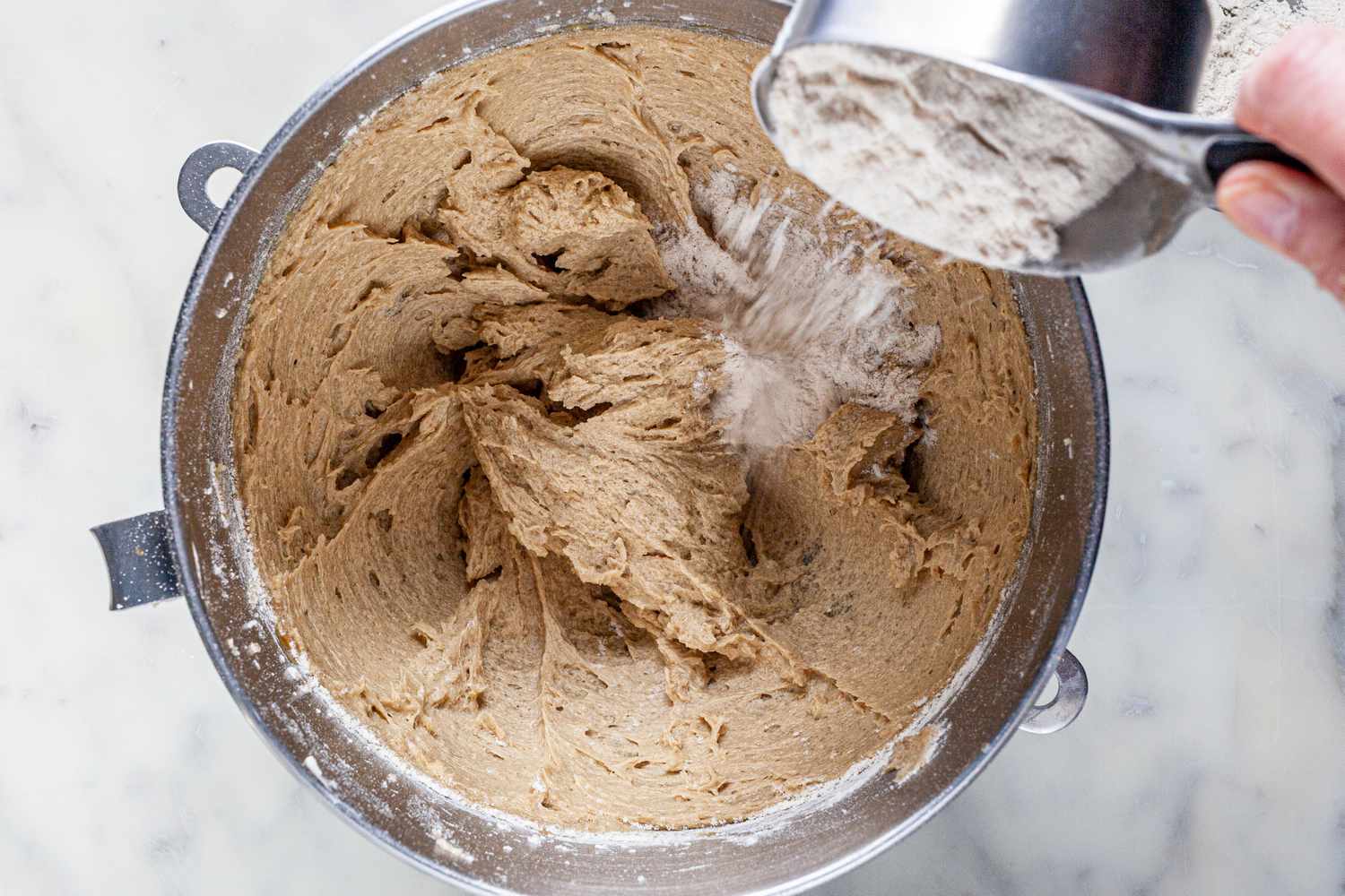 Adding dry ingredients to a bowl of creamed eggs, sugar, and butter to make cowboy cookies