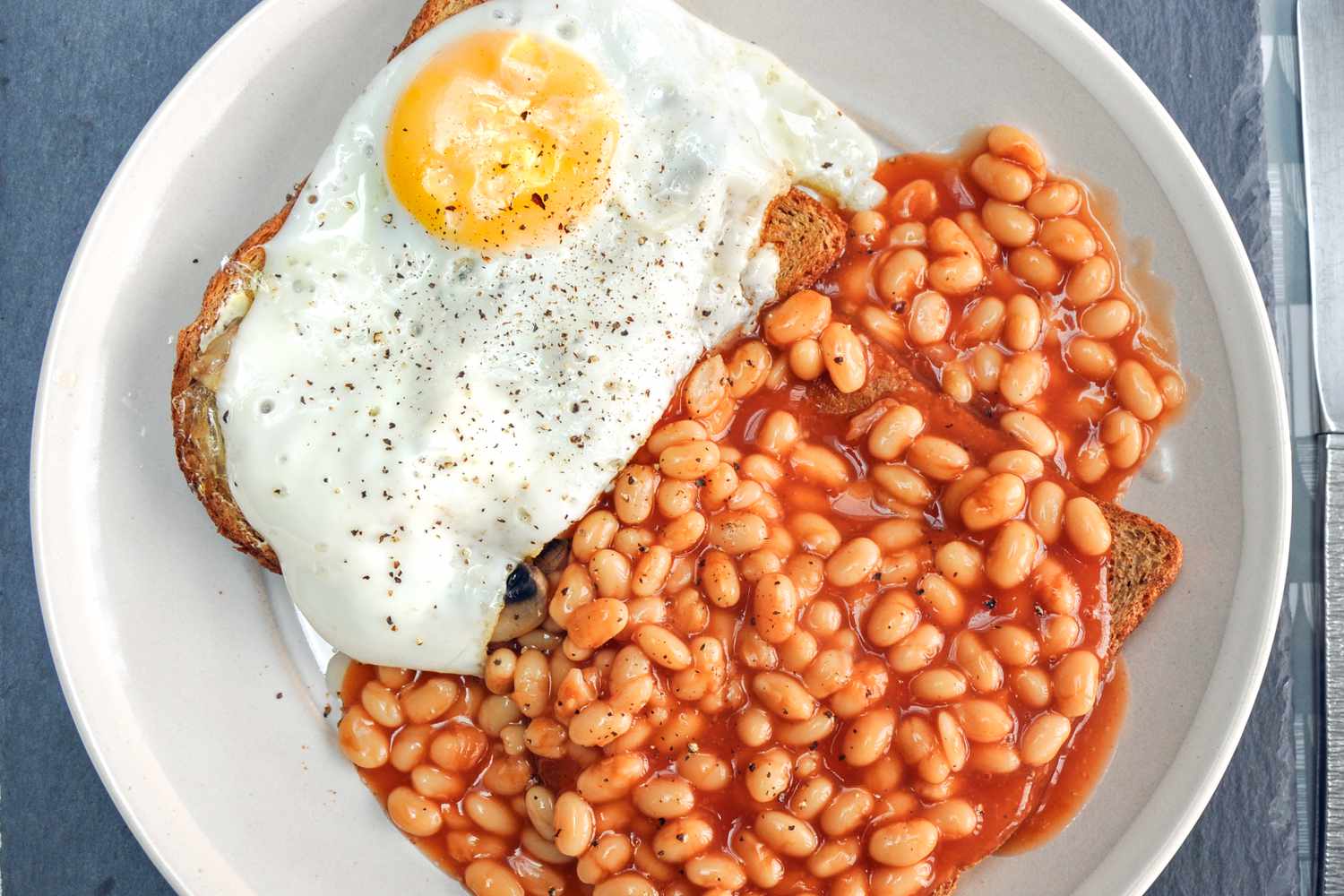 baked beans and a sunny sied egg over slices of bread on a plate