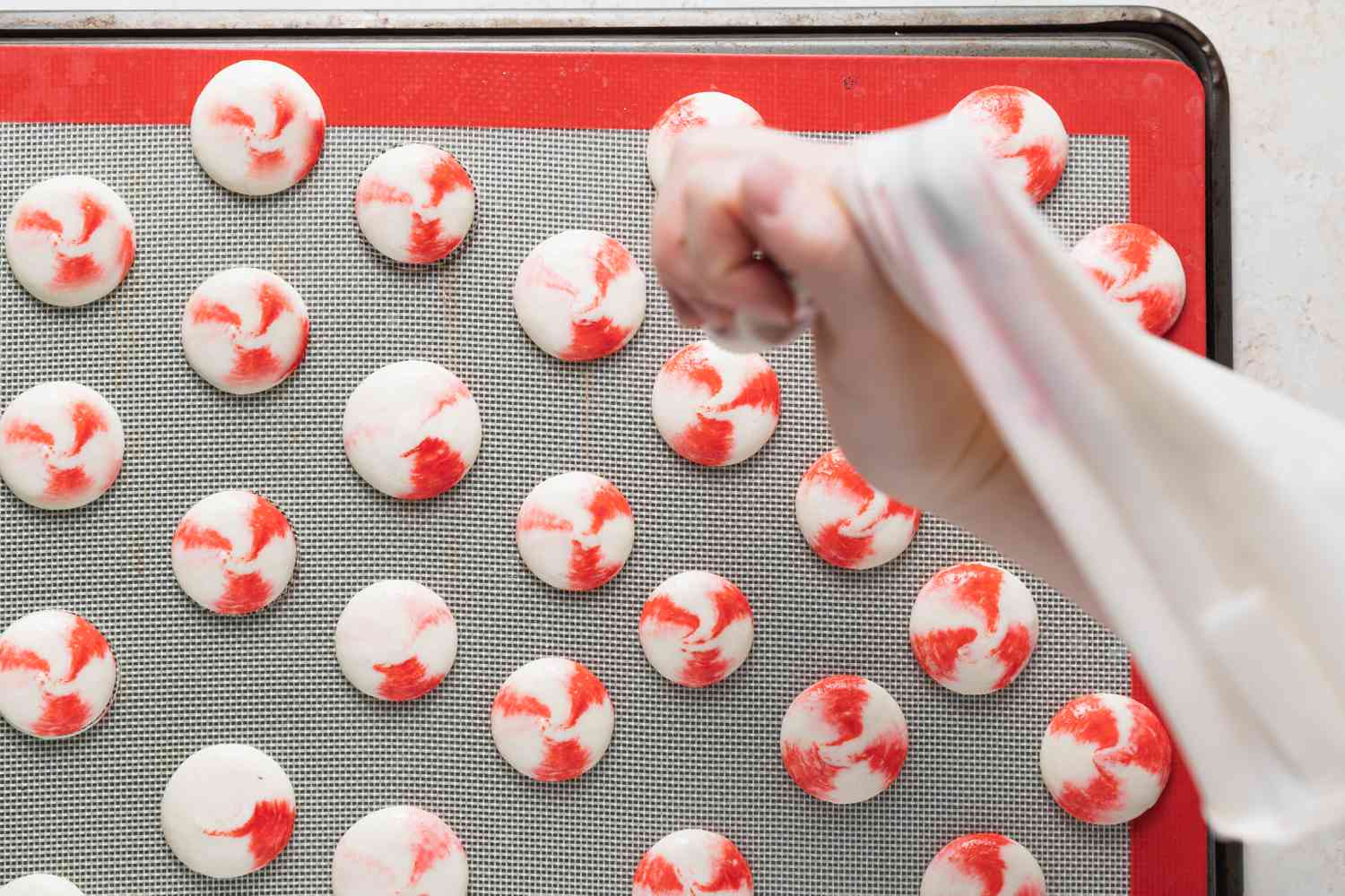 Piping macaron shells onto a lined baking sheet to make French macarons with peppermint white chocolate filling
