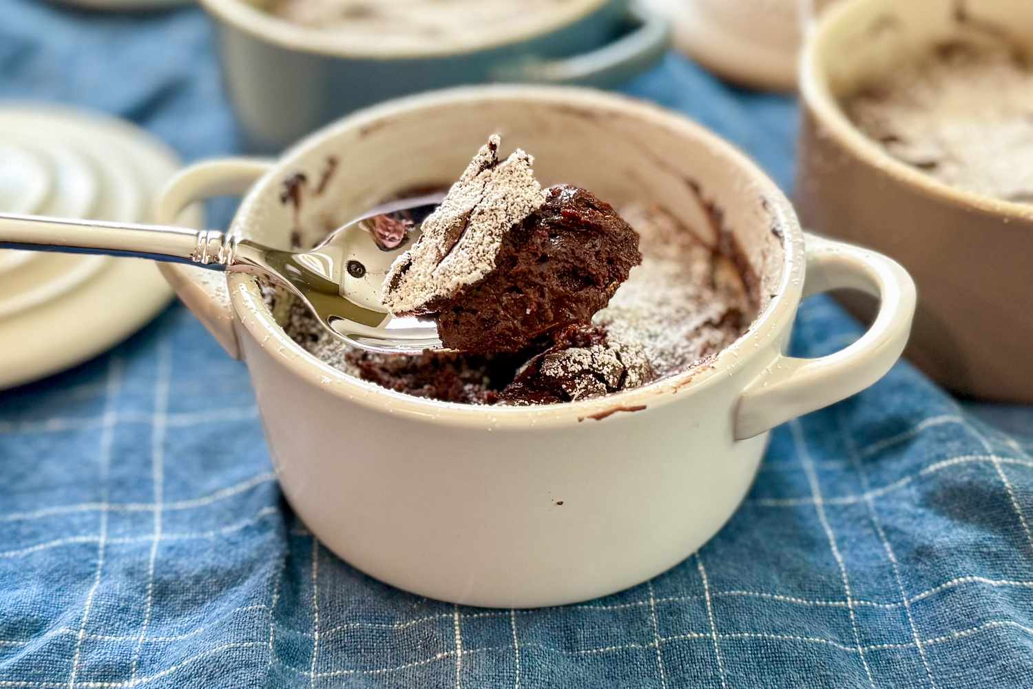 Small bowl of Meghan Markle's Molten Chocolate Cakes recipe with a serving on a spoon all on a blue plaid cloth