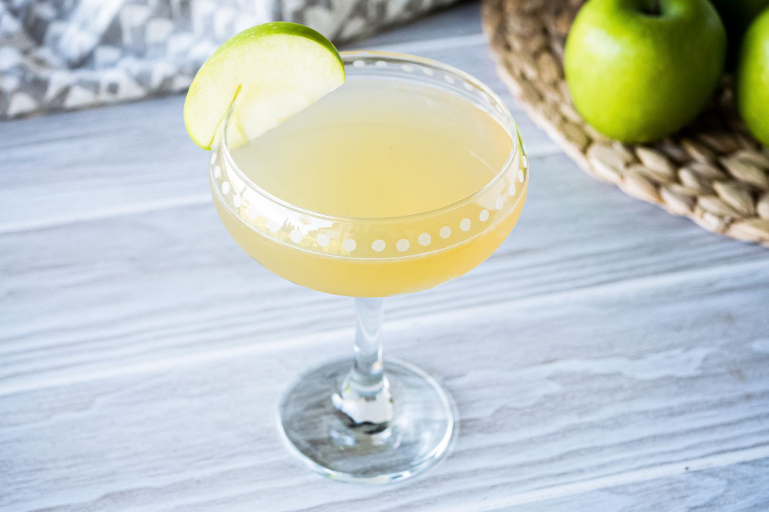 Appletini cocktail garnished with a thin slice of green apple.