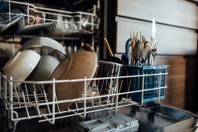 A dishwasher filled with bowls, plates, glasses, and silverware. 