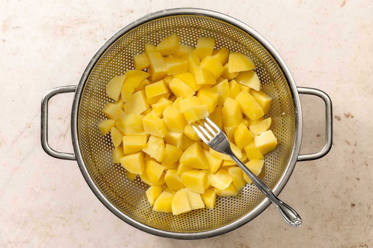 overhead view of cooked chopped potatoes in a strainer for Chantilly Potatoes recipe