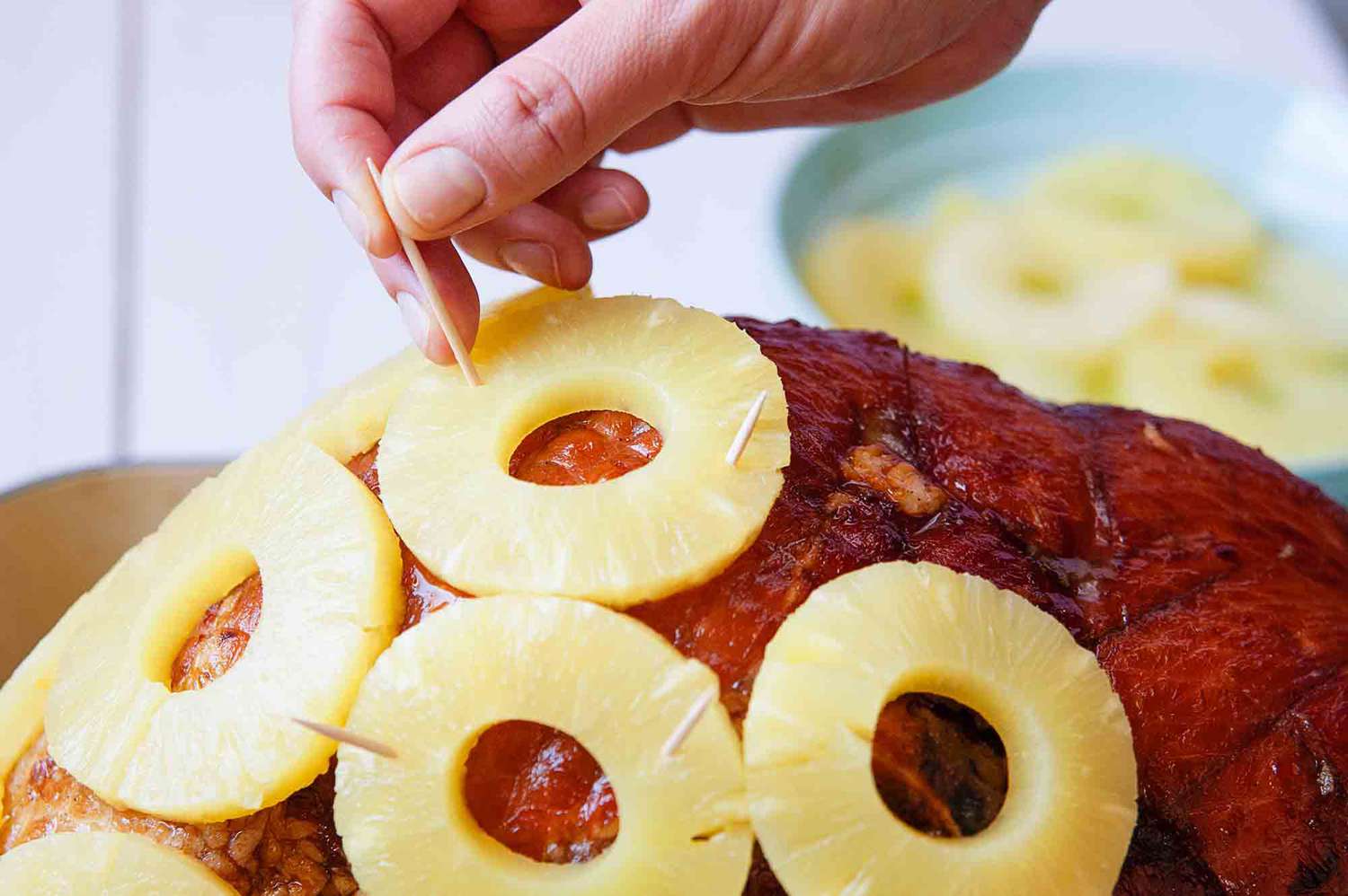 Baked Ham Recipe with Brown Sugar - person securing pineapple rings to ham with toothpicks