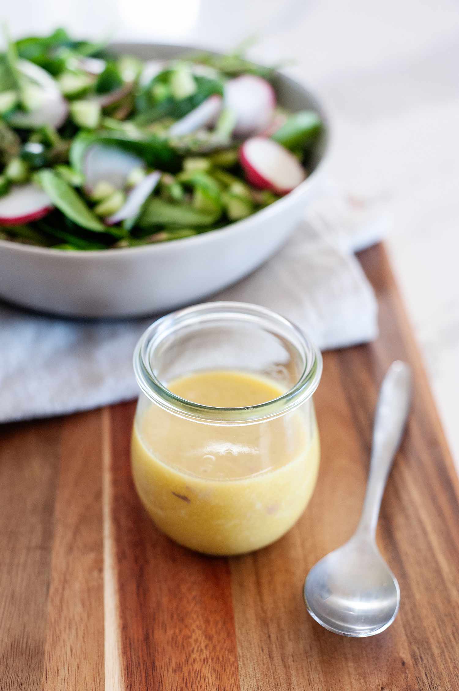Anchovy Mustard Salad Dressing in a jar next to a salad.
