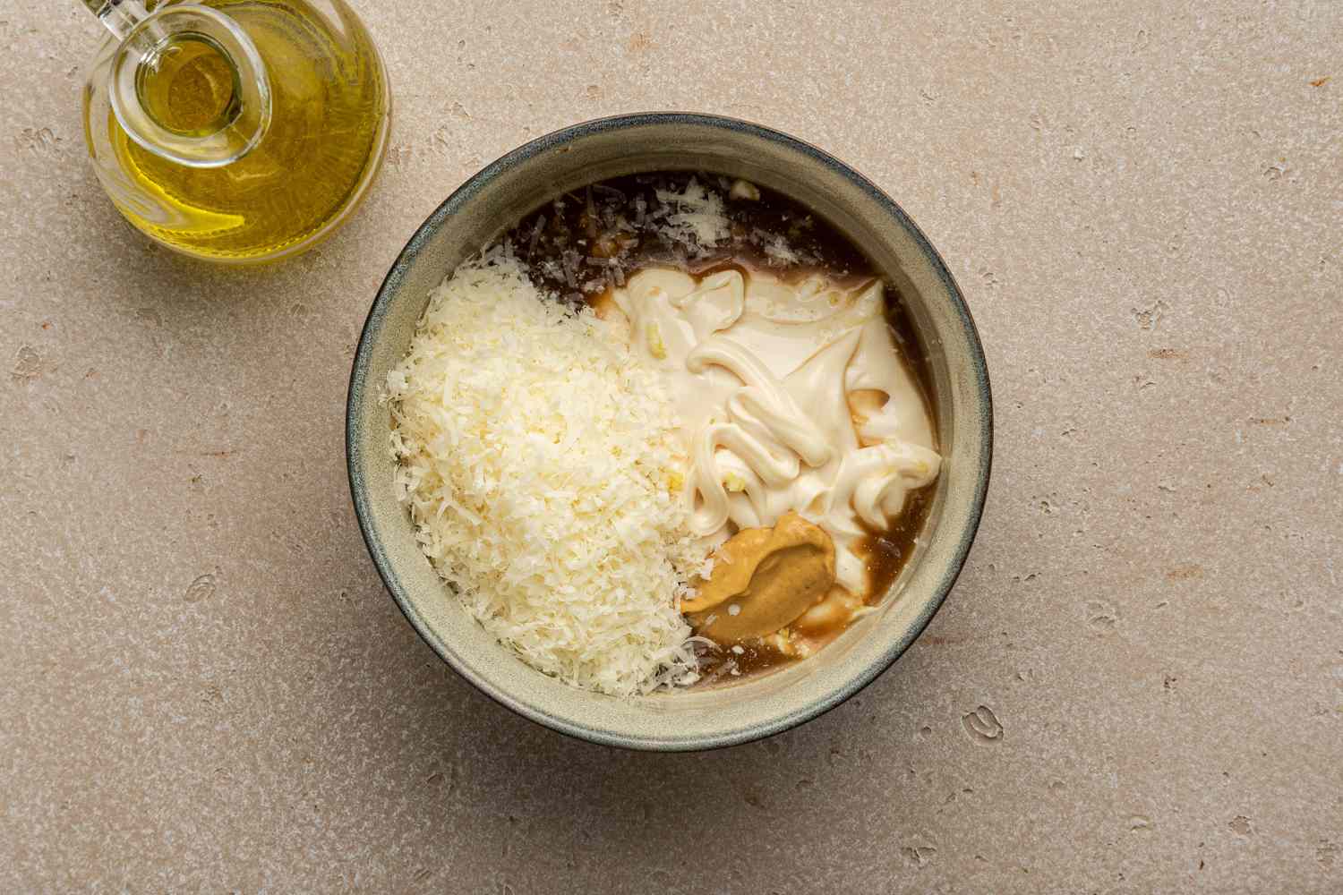 Bowl of Caesar Sauce Ingredients (Parmesan, Mayonnaise, Dijon Mustard, Garlic, Lemon Juice, and Worcestershire sauce) Next to a Oil Holder 