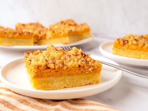 Pumpkin Cream Cheese Bars on a platter in the background, 2 plates with one bar each