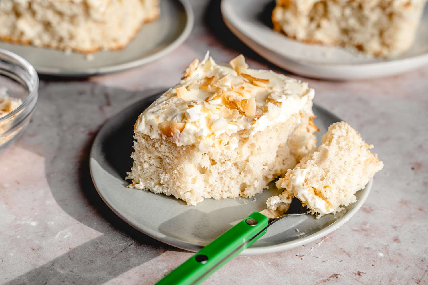 Angled view of a gray plate of coconut cake with a fork on a gray countertop