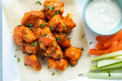 Air Fryer Buffalo Cauliflower Bites topped with sauce and next to a bowl of dip, carrots, and celery.