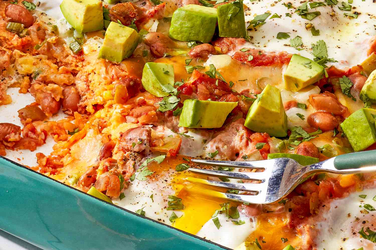 Close-up: huevos rancheros casserole in a casserole dish with an egg yolk poked with a fork
