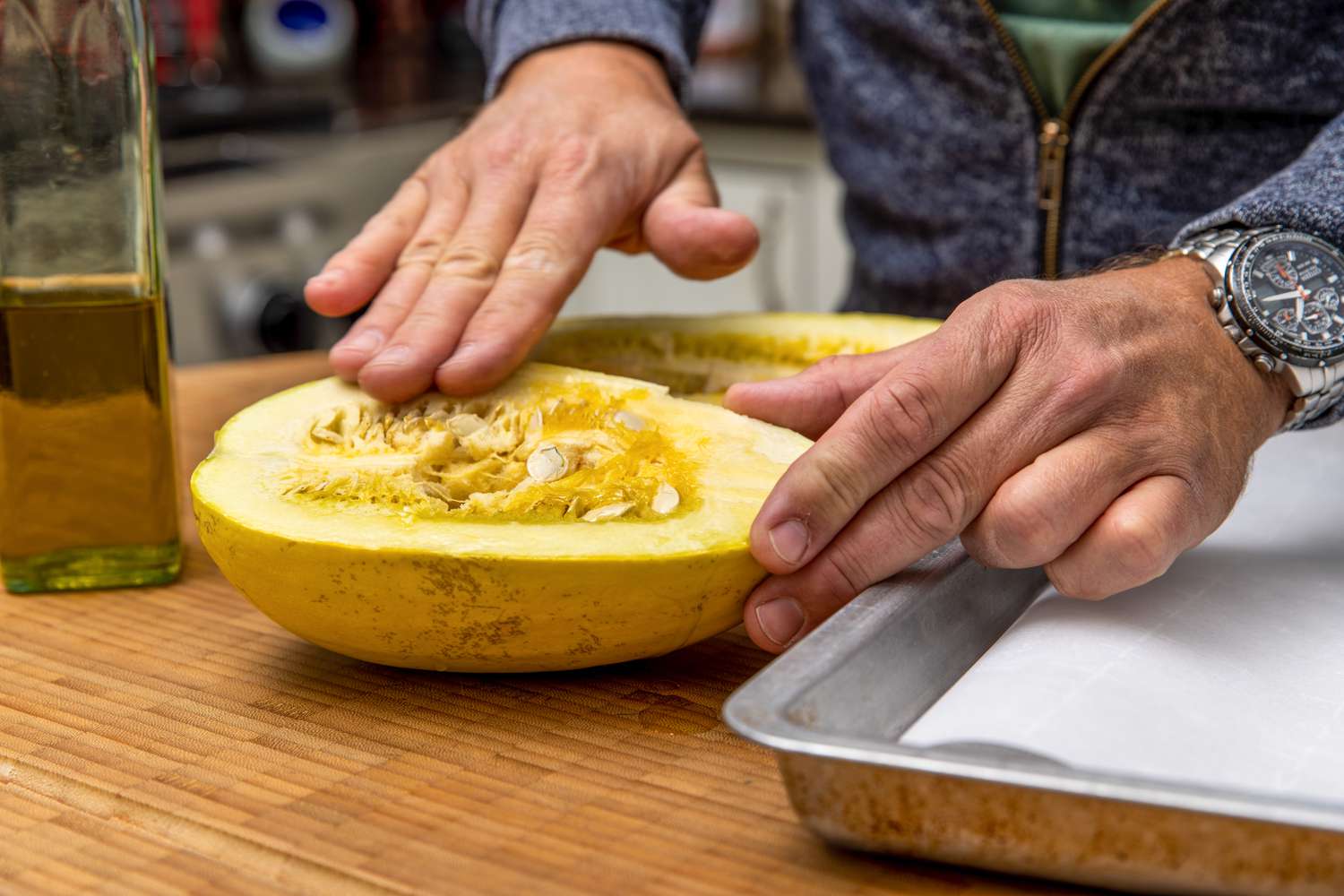 Fingers Spreading Olive Oil onto Flesh Side of Halved Spaghetti Squash for Spaghetti Squash Soup Recipe