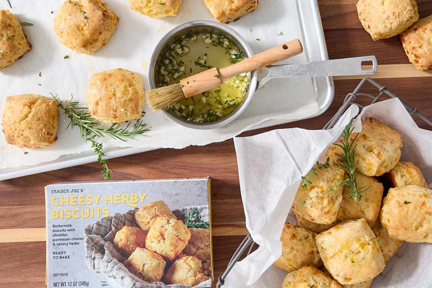 Trader Joe's Cheesy Herby Biscuits in a box and several baked on a sheet pan, with a small pot of garlic herb sauce with a brush, some biscuits in a basket