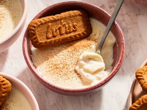 Dessert in a bowl topped with a spiced cookie and sprinkled with spice served with a spoon