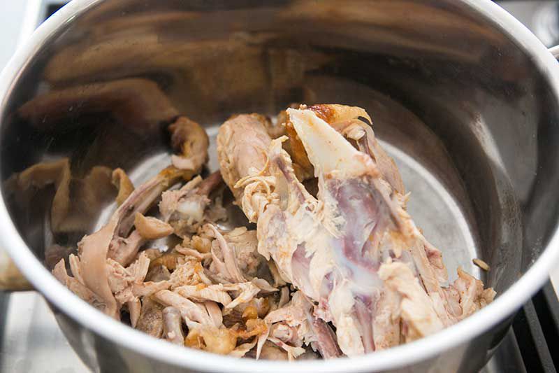 A cut up chicken carcass in a stock pot