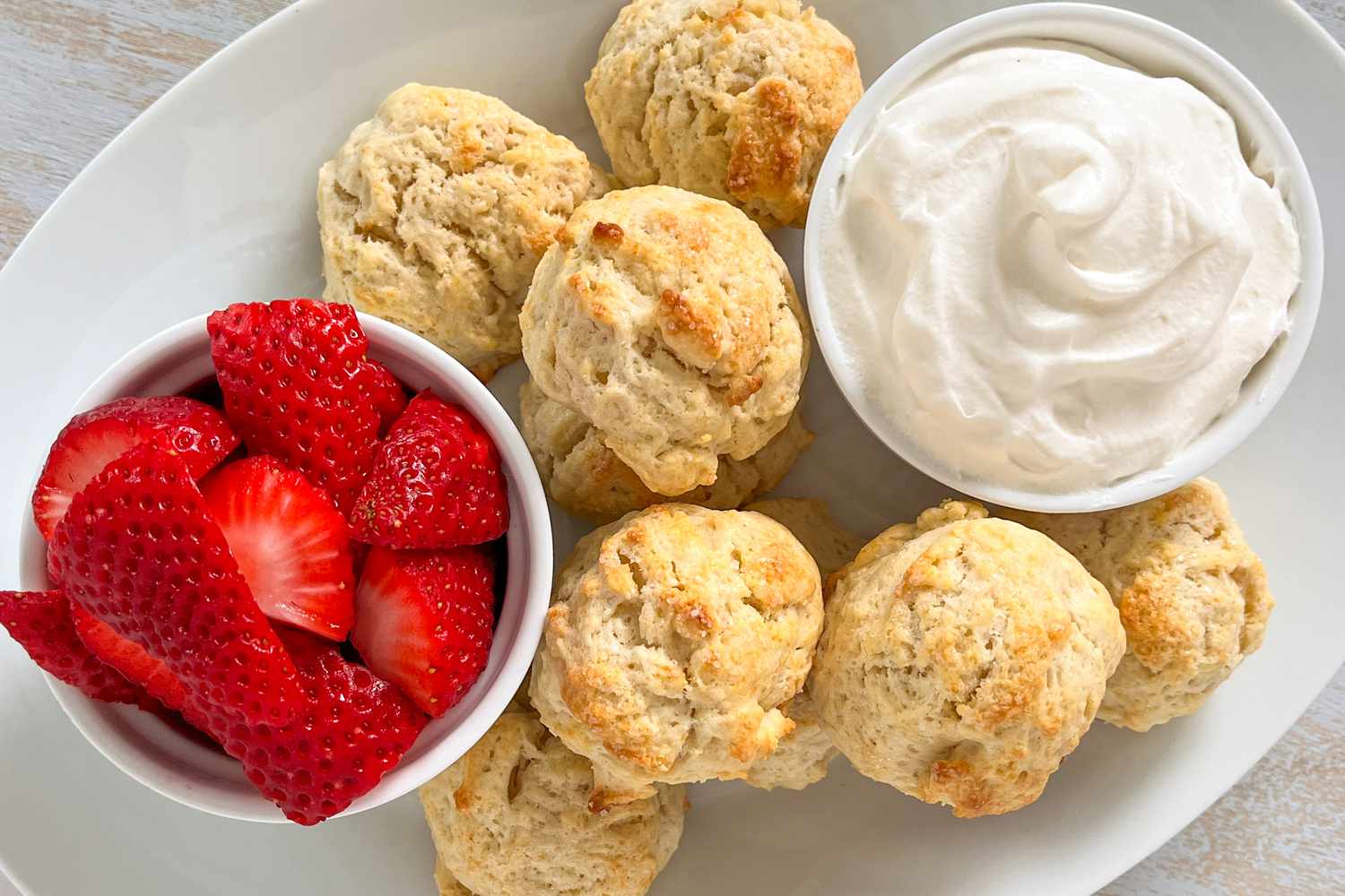 2-ingredient biscuits, a bowl of cut strawberries, and a bowl of whipped cream on a platter