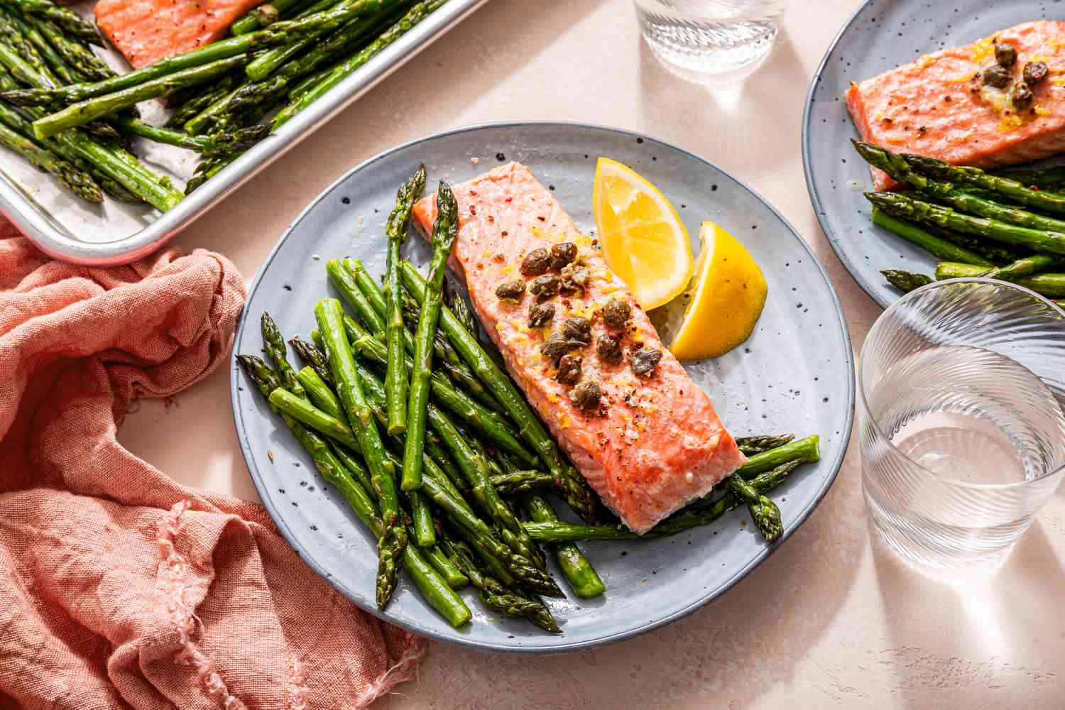 Sheet pan salmon and asparagus served on blue plates with lemon wedges