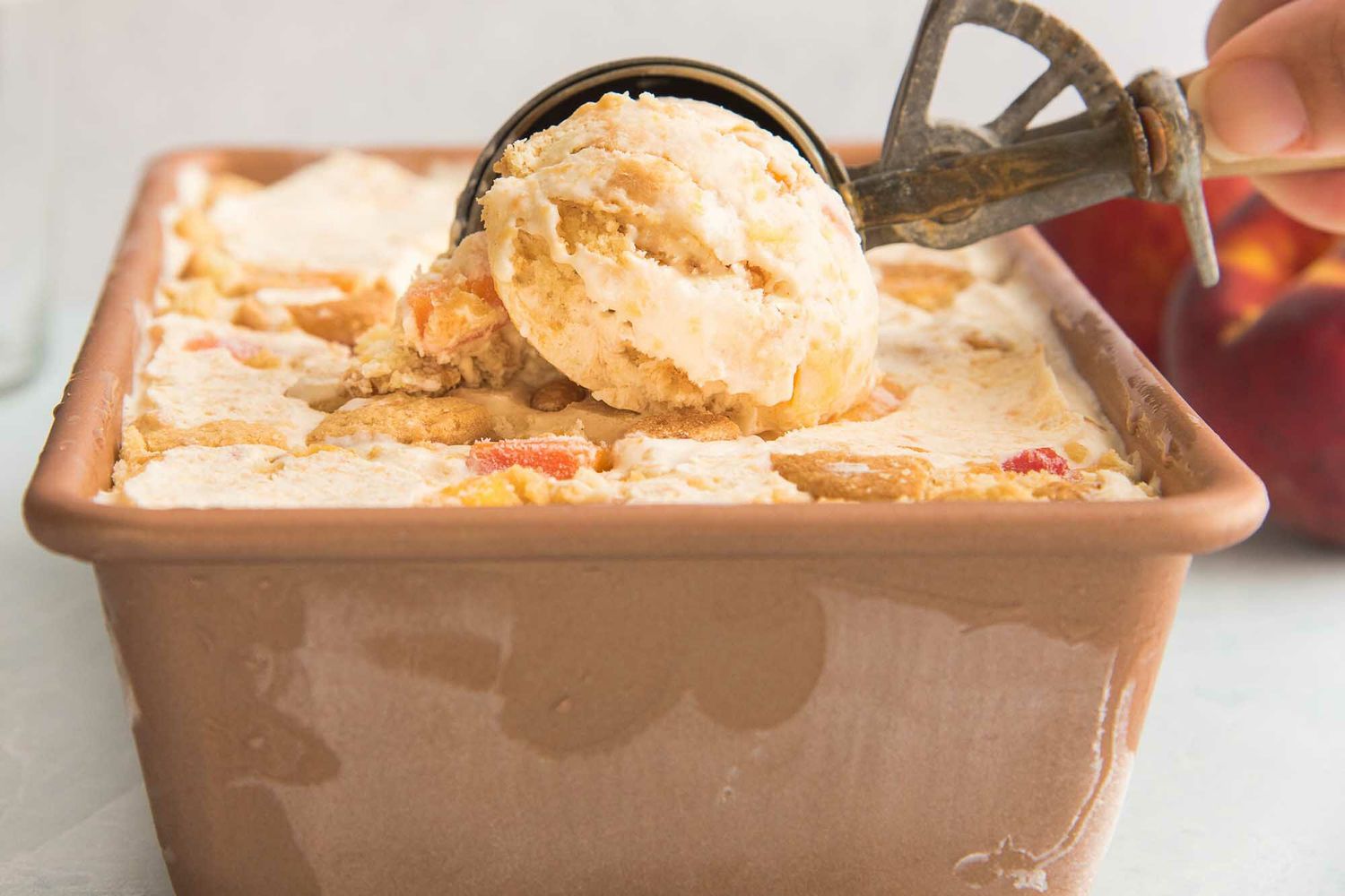 Peach cobbler ice cream is being scooped and chopped peaches are visible.