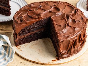 black magic cake on a platter with a slice cut out and in the background, two plates with some cake slices