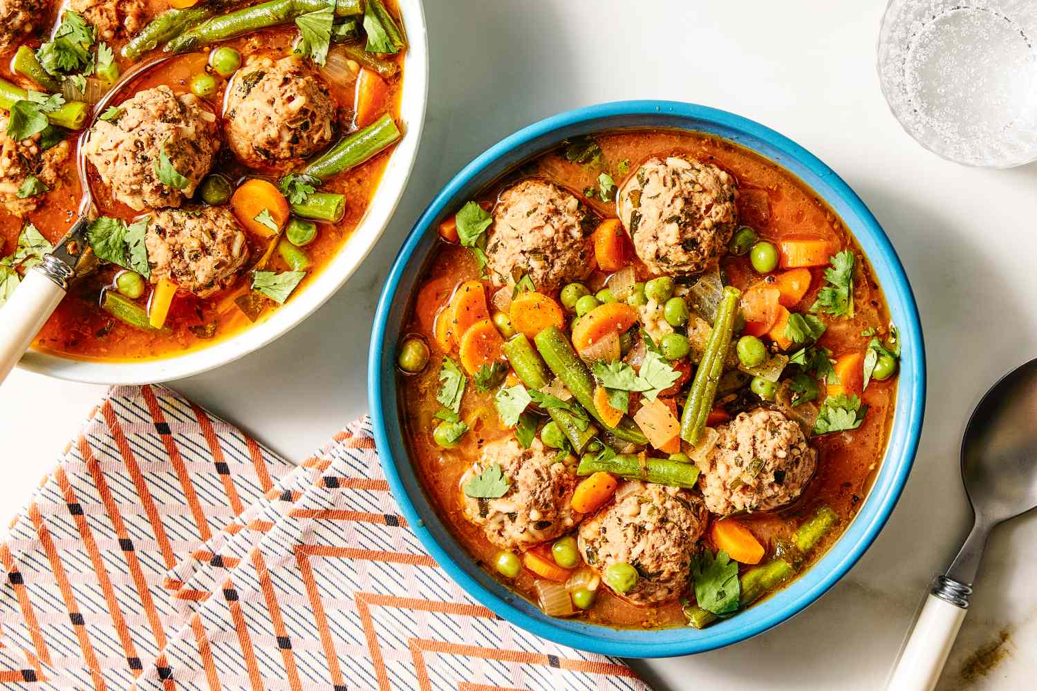 Two bowls of albondigas soup with meatballs and vegetables a patterned napkin and cutlery nearby