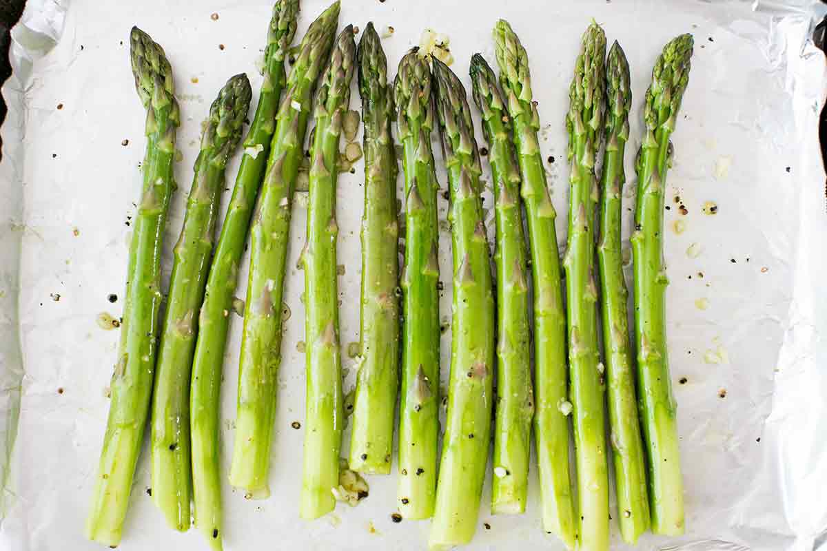 Asparagus lined up on a foiled baking sheet with salt, pepper, and olive oil drizzled on top 