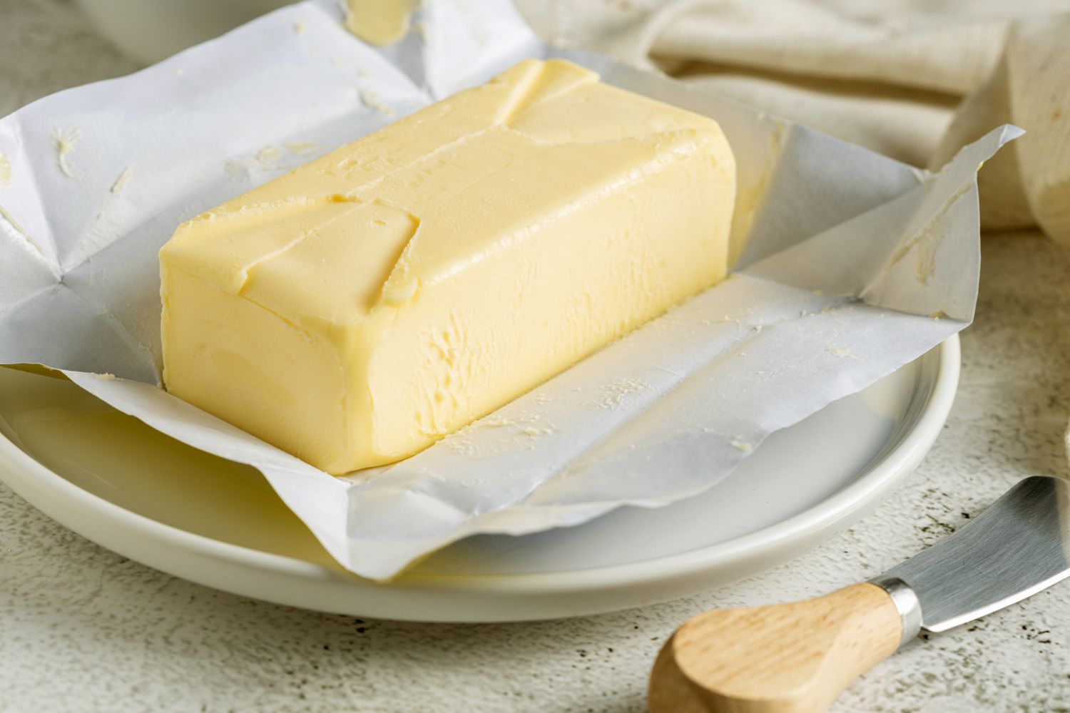 Stick of butter partially unwrapped on a plate butter knife nearby