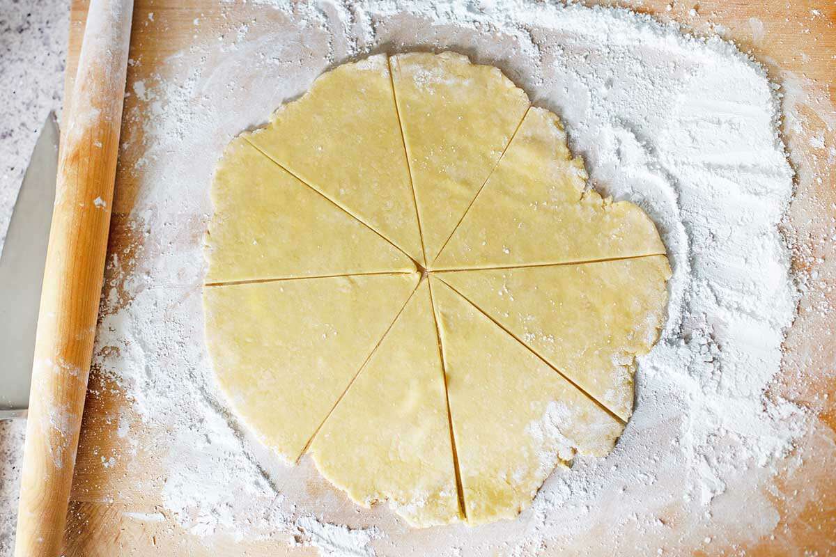 A circle of dough rolled on a floured counter and cut into triangles to make Butterhorn Cookies Filled with Walnut Meringue.