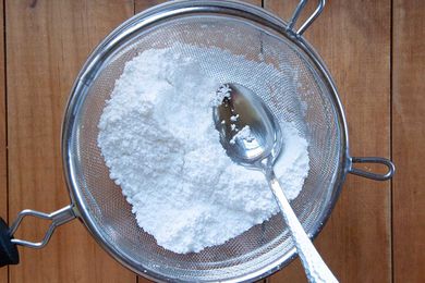 Powdered sugar in a sifter is being pressed with a spoon.
