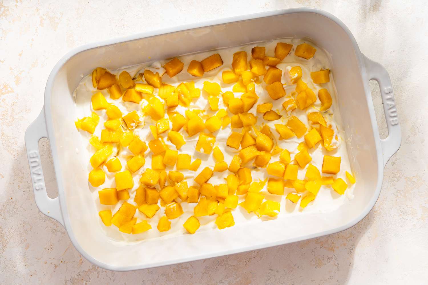 first layer of whipped cream and chopped mangoes added to baking dish for mango royale recipe