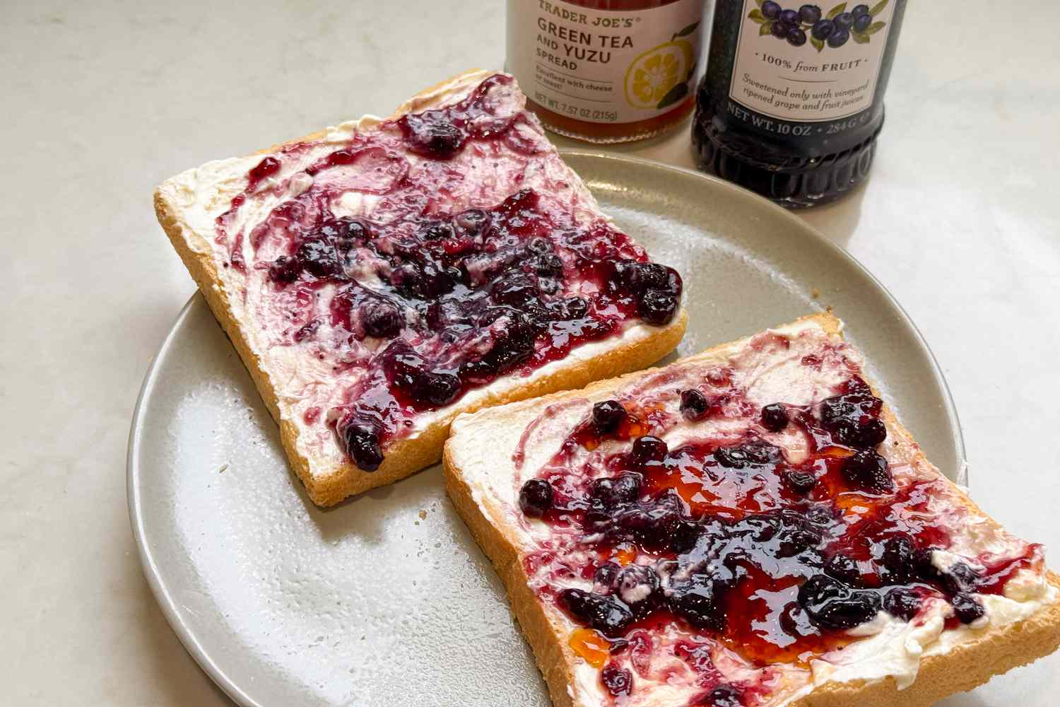 Side shot of two toasts in a plate topped with cream cheese and blueberry jam