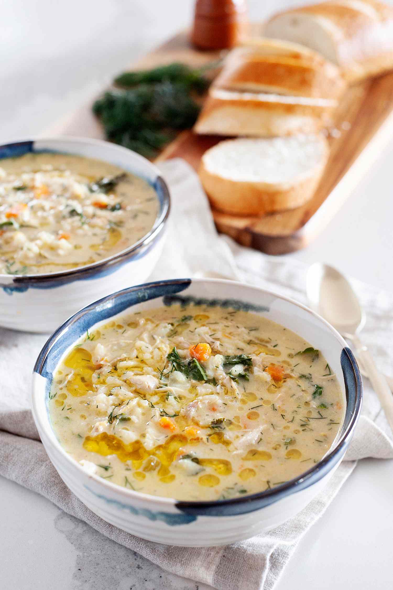 Avgolemono in a bowl with a second bowl and sliced bread behind it.