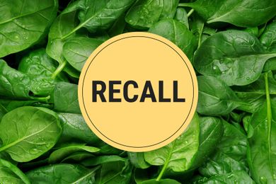 A recall notice overlaid on fresh spinach leaves