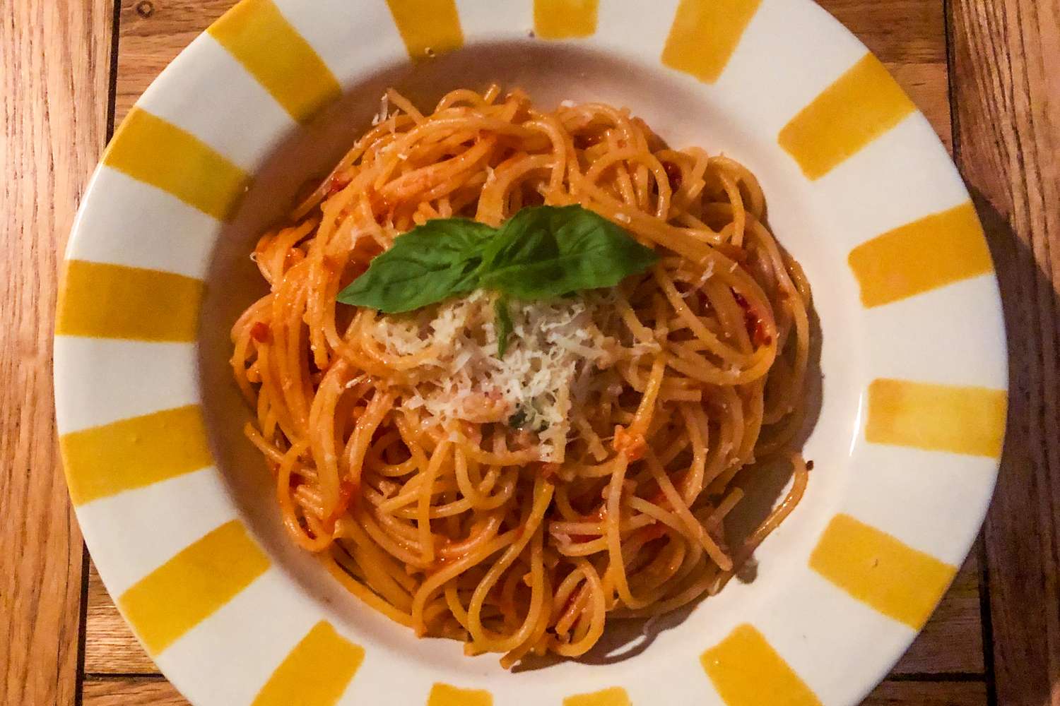A plate of spaghetti arrabbiata with grated cheese and basil leaf garnish