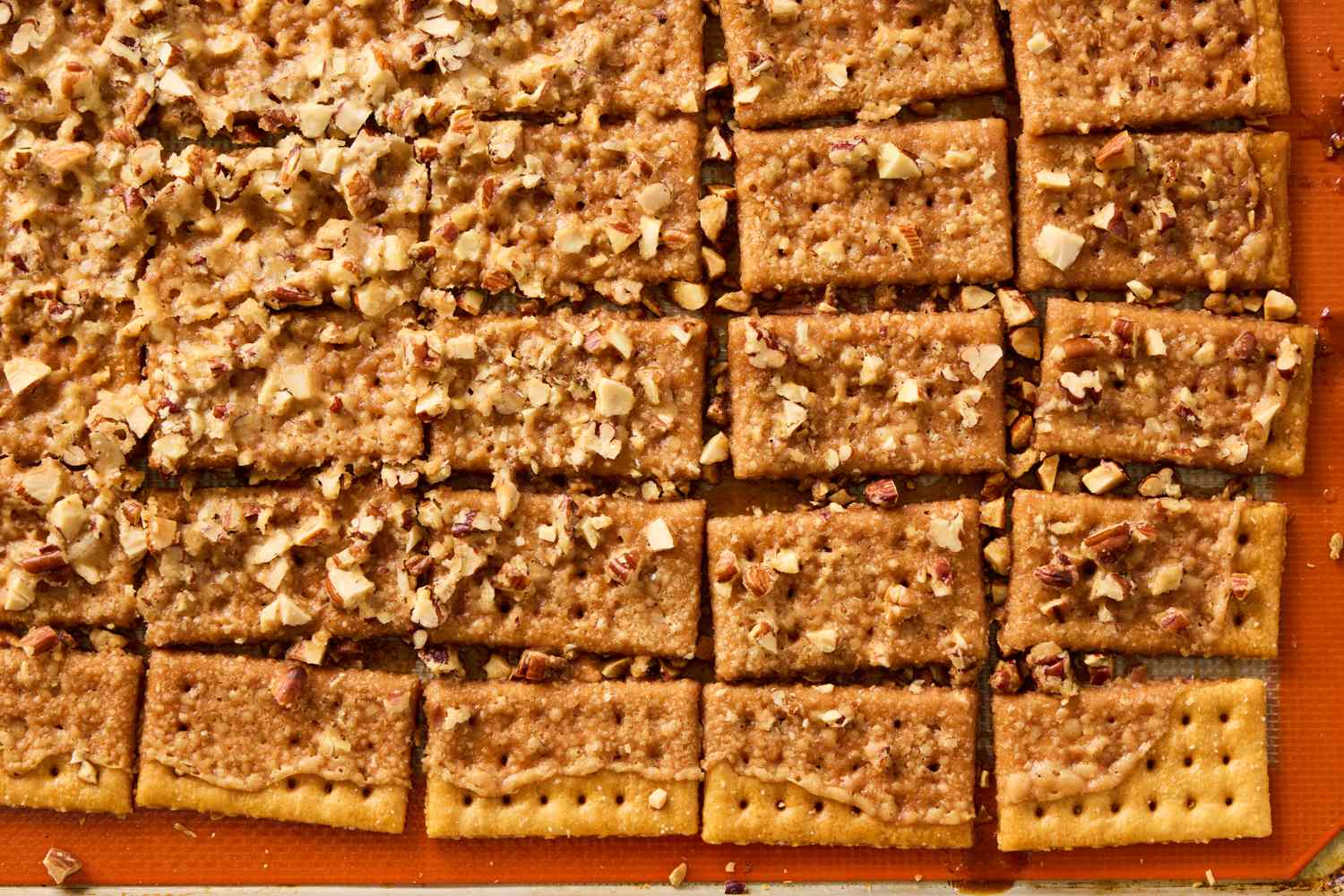 Club crackers arranged with a topping of chopped nuts and a caramelized layer on a baking sheet
