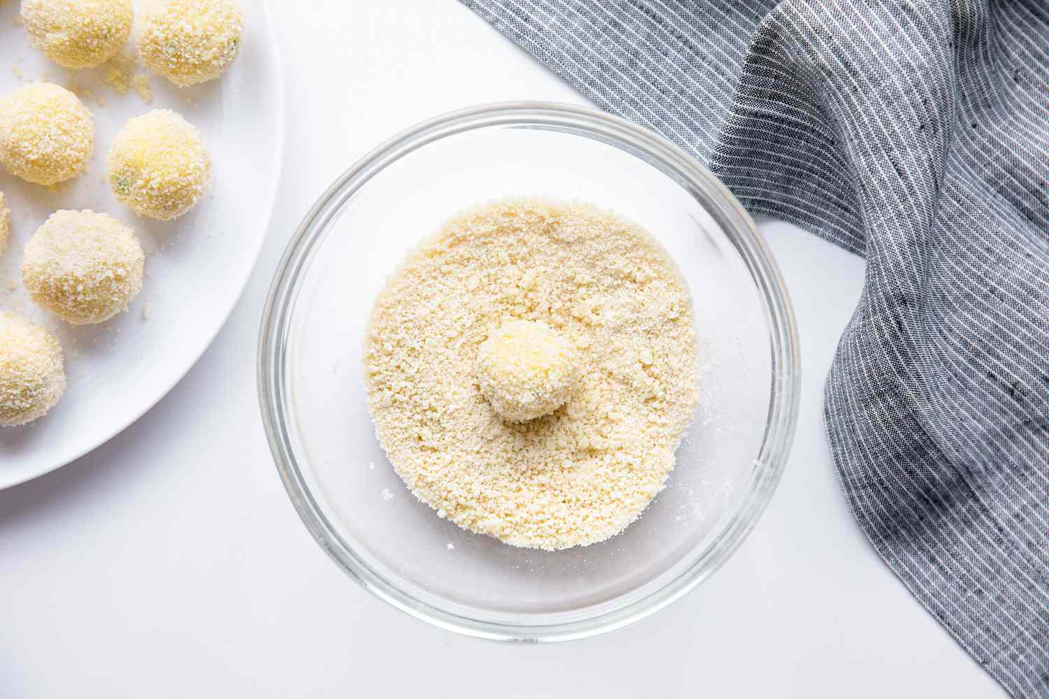 Dredging Step: Potato Croquette Ball in a Bowl of Breadcrumbs Next to a Plate of Breaded Croquettes