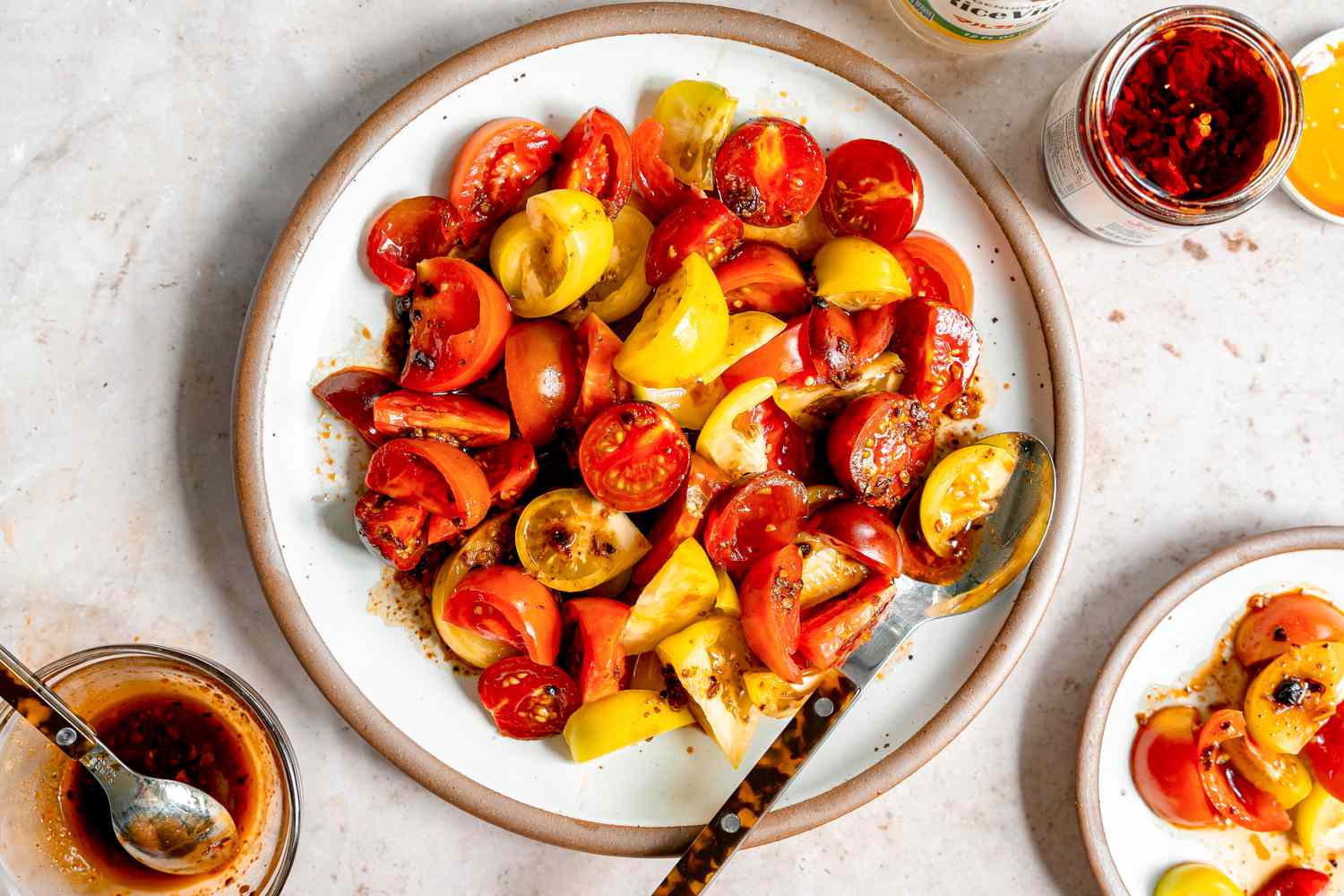 5-minute chili crisp tomato salad on a plate next to a small plate with a serving, a bowl of chili crisps, and a jar with more chili crisp