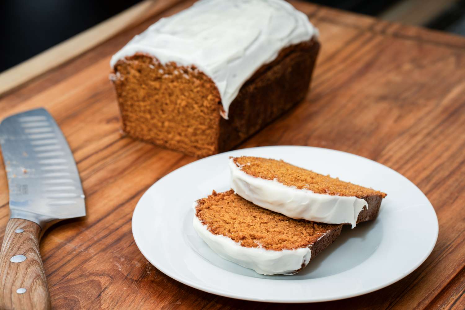 Loaf of frosted cake with two slices on a plate knife on the wooden surface