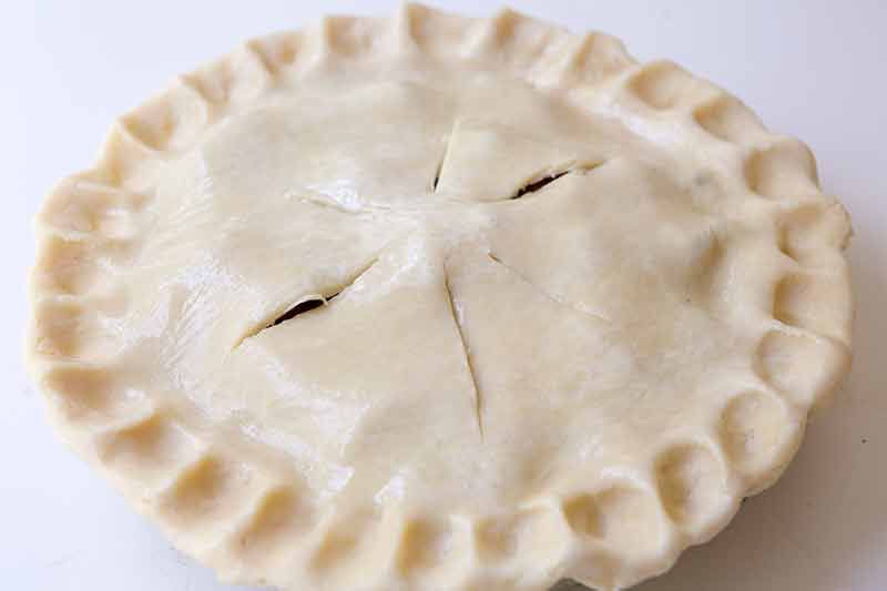 top the strawberry rhubarb filling with the top crust, crimp the edges and make vents