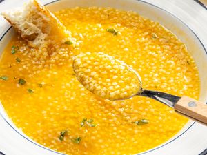 A bowl of pastina in brodo with a spoon and a piece of crusty bread