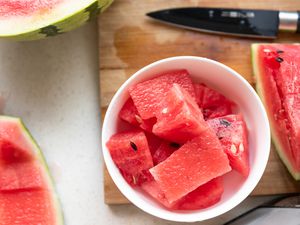 A bowl of cut watermelon over a cutting board with pieces of cut watermelon and a paring knife