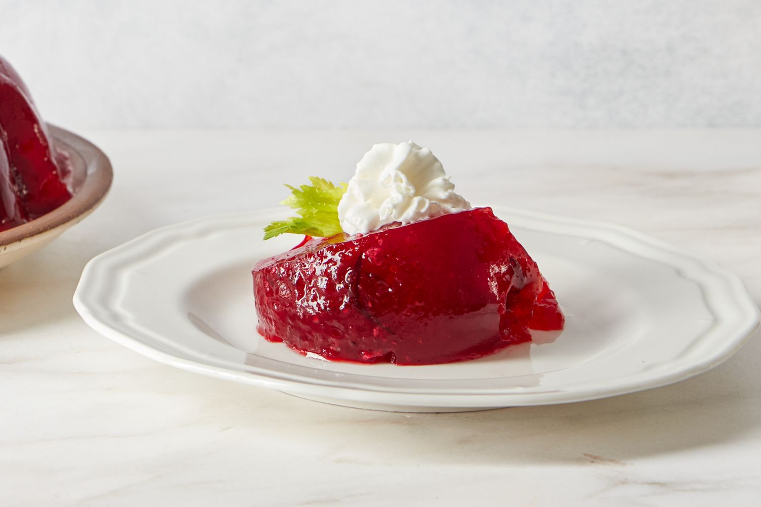 A slice of cranberry salad topped with whipped cream on a plate