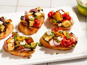 Toasts topped with grilled summer vegetables, goat cheese, and pesto on a white serving platter
