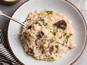 A bowl of mushroom risotto with a spoon scooping risotto out of the bowl.