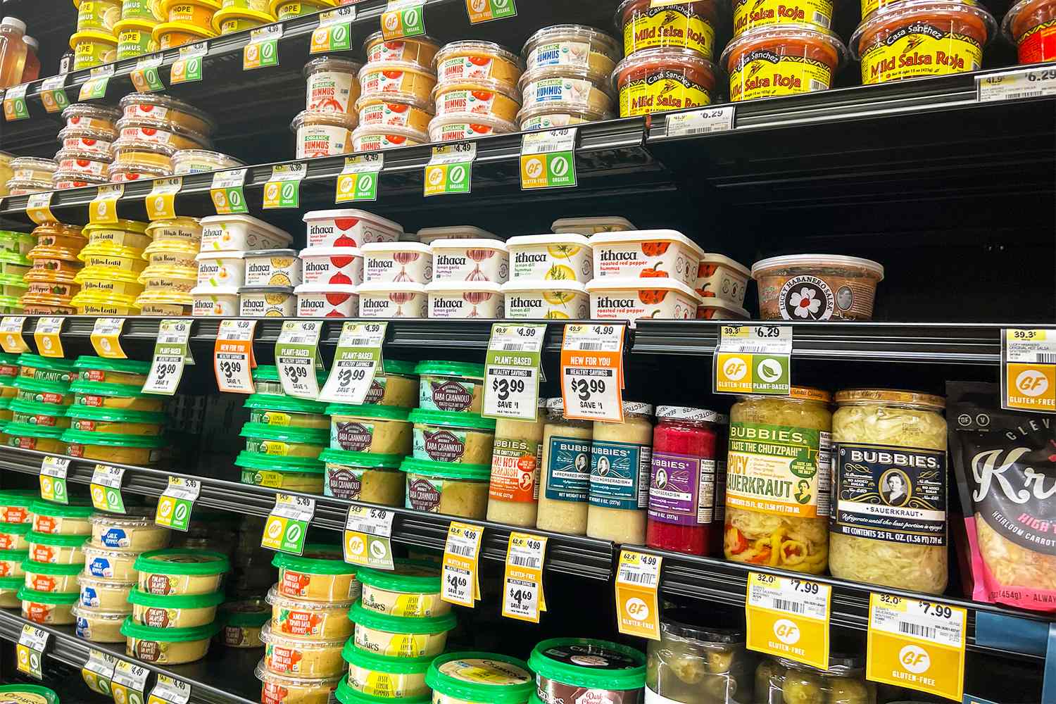 A grocery store shelf displaying various brands of hummus and dips
