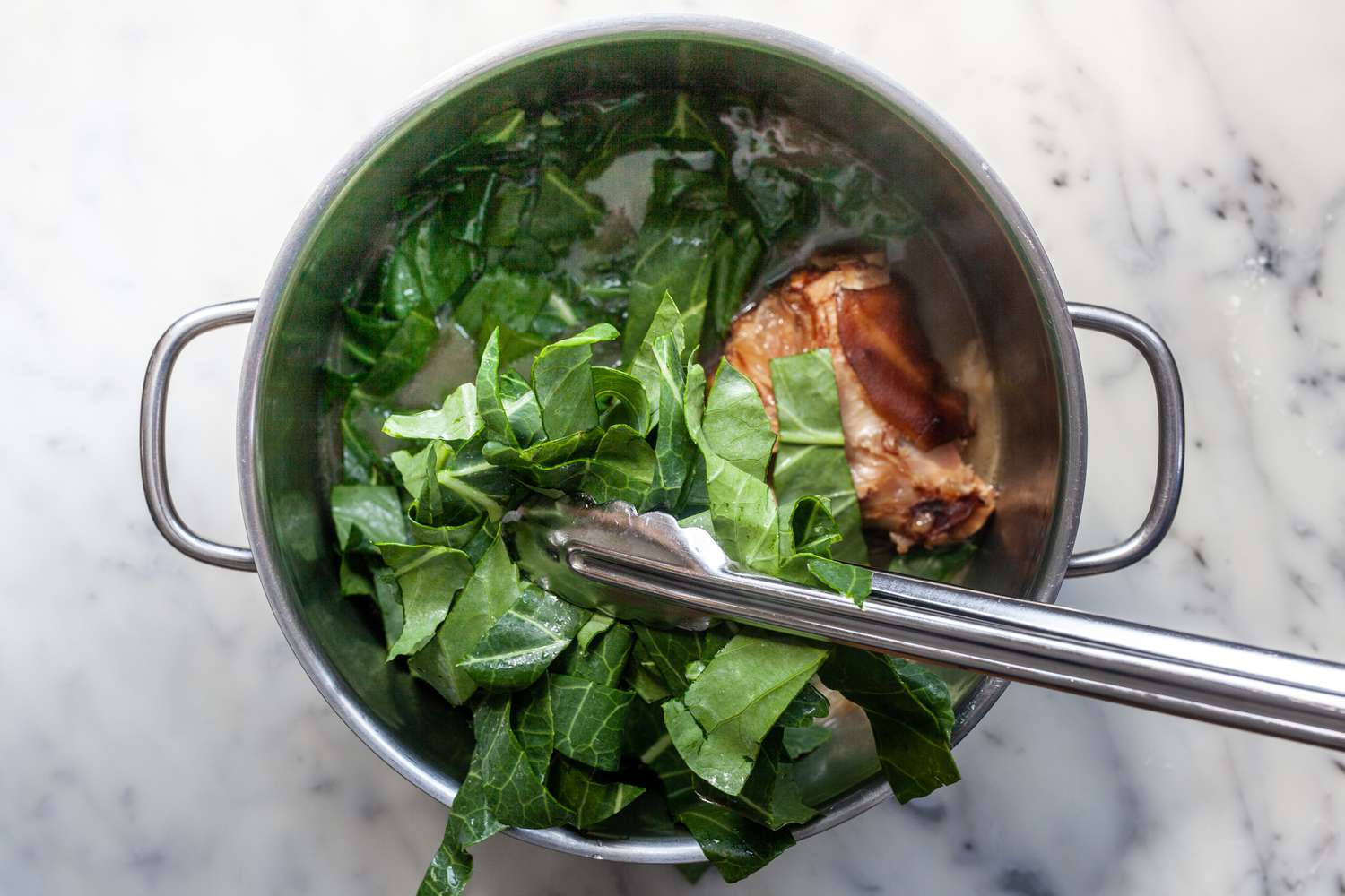 Adding greens to a stockpot for a southern collard greens recipe.