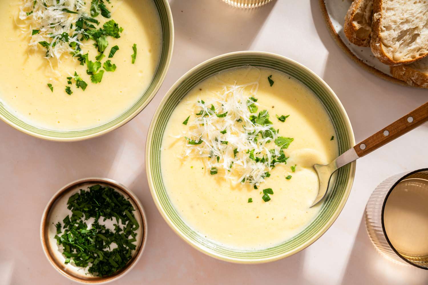 Bowls of creamy potato soup garnished with herbs and grated cheese served with bread slices on the side