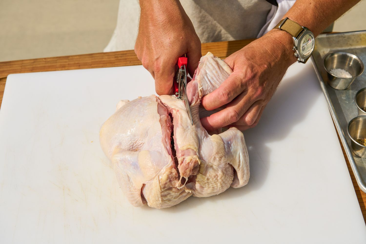 A person using kitchen shears to cut a raw chicken in half on a cutting board for Grilled Half Chicken recipe