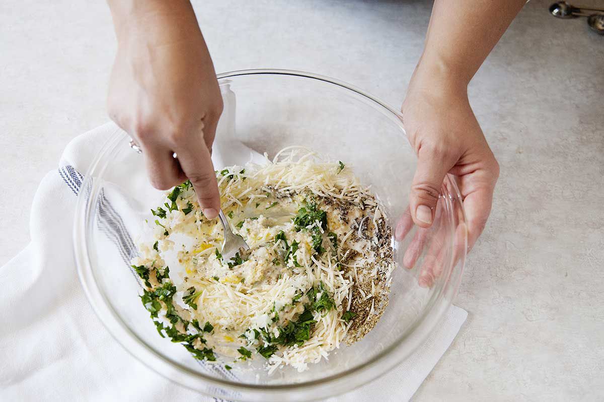 Eggs, breadcrumbs, herbs and cheese in a bowl being stirred together.